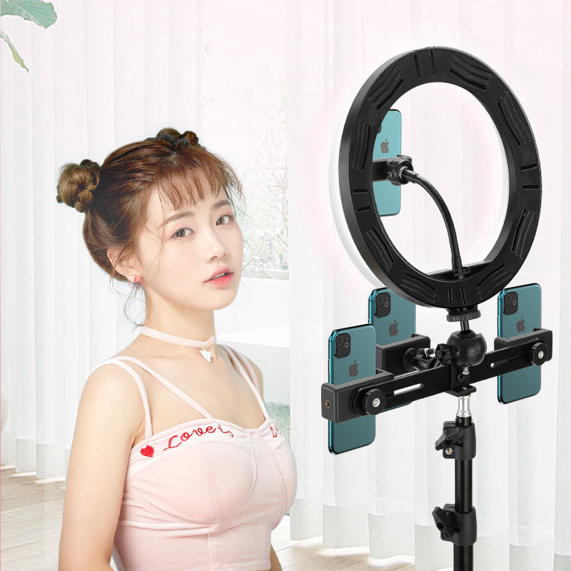 Woman with a ring light and smartphone holder in a room with white curtains.