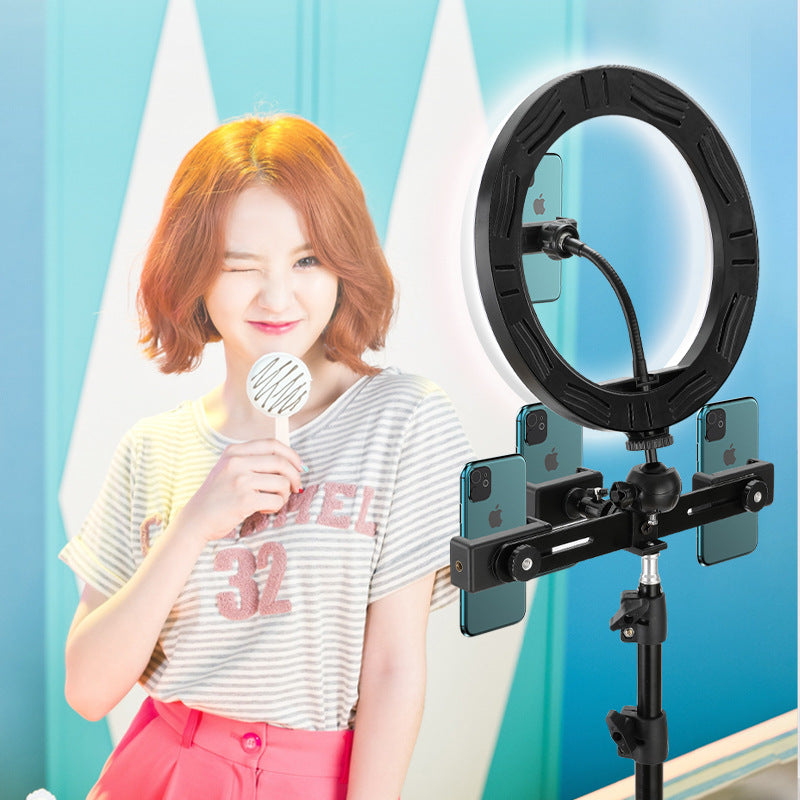 Woman holding a microphone with a ring light and smartphone holder on a stand against a blue curtain background.