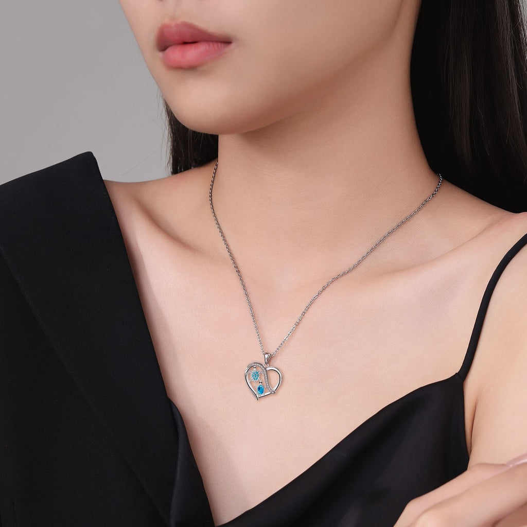 Woman wearing a silver necklace with a heart-shaped pendant against a neutral background